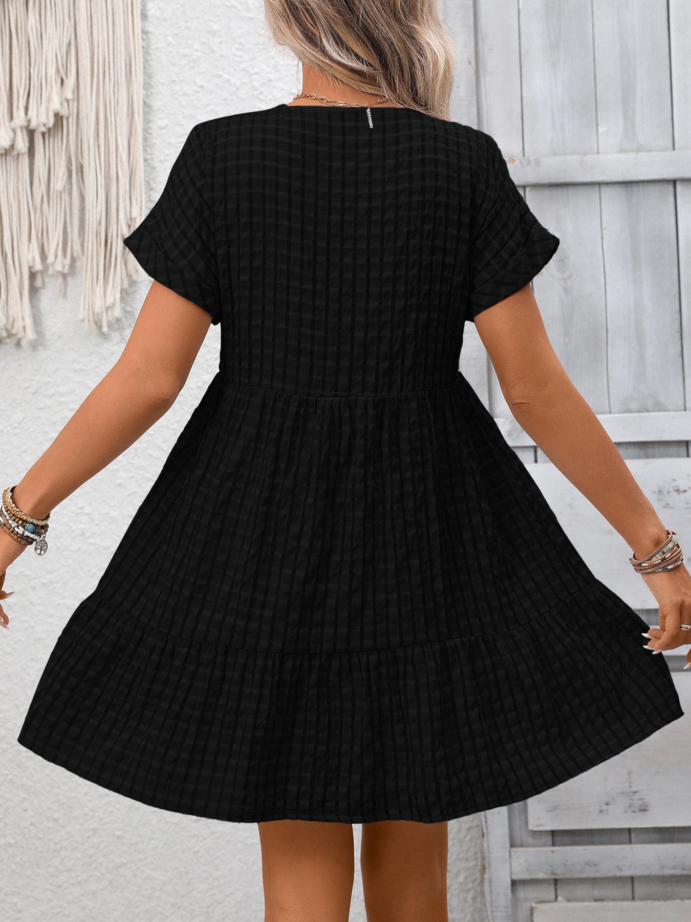 Black checkered dress worn by a person against a light gray wall.