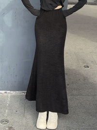 Person wearing a black ribbed knit skirt on a gray pavement.