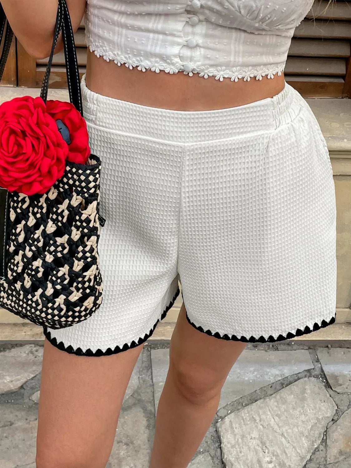 Person wearing white shorts with black trim, holding a black and white patterned bag with a red flower.