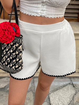 Person wearing white shorts with black trim, holding a black and white patterned bag with a red flower.