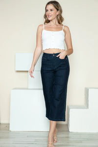Woman wearing a white top and dark blue jeans standing against a light background