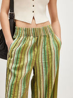 Person wearing green and brown striped pants with a white top on a plain background