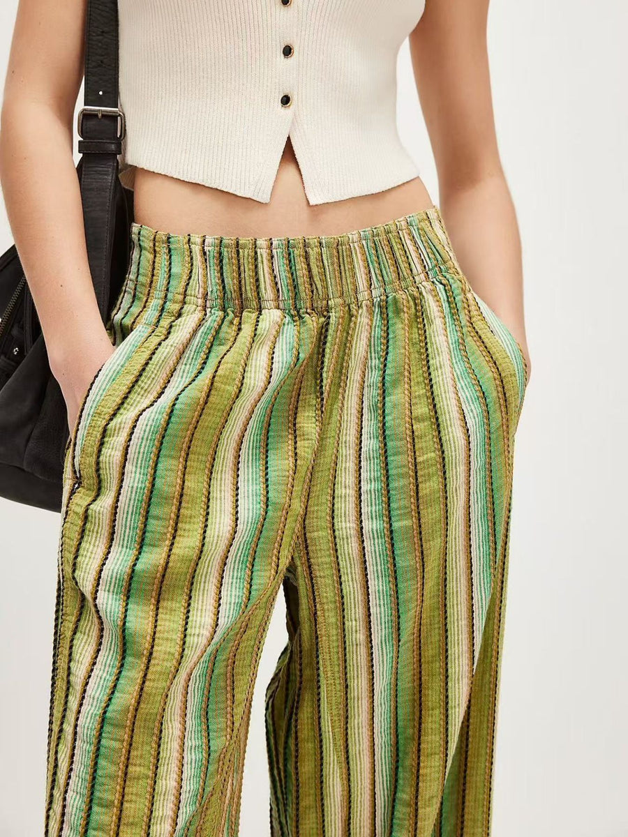 Person wearing green and brown striped pants with a white top on a plain background