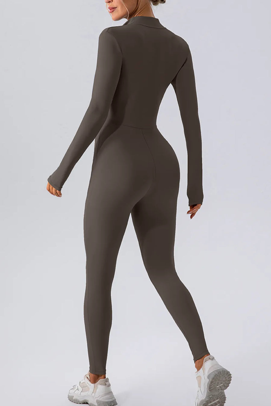 Person wearing a brown long-sleeve jumpsuit on a light gray background