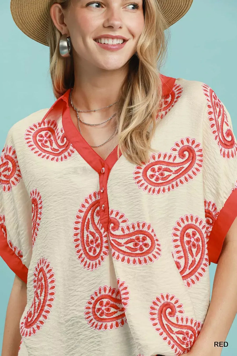 Woman wearing a cream blouse with red paisley patterns and a straw hat against a light blue background