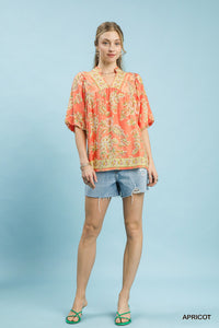 Woman wearing a patterned orange shirt and denim shorts on a light blue background