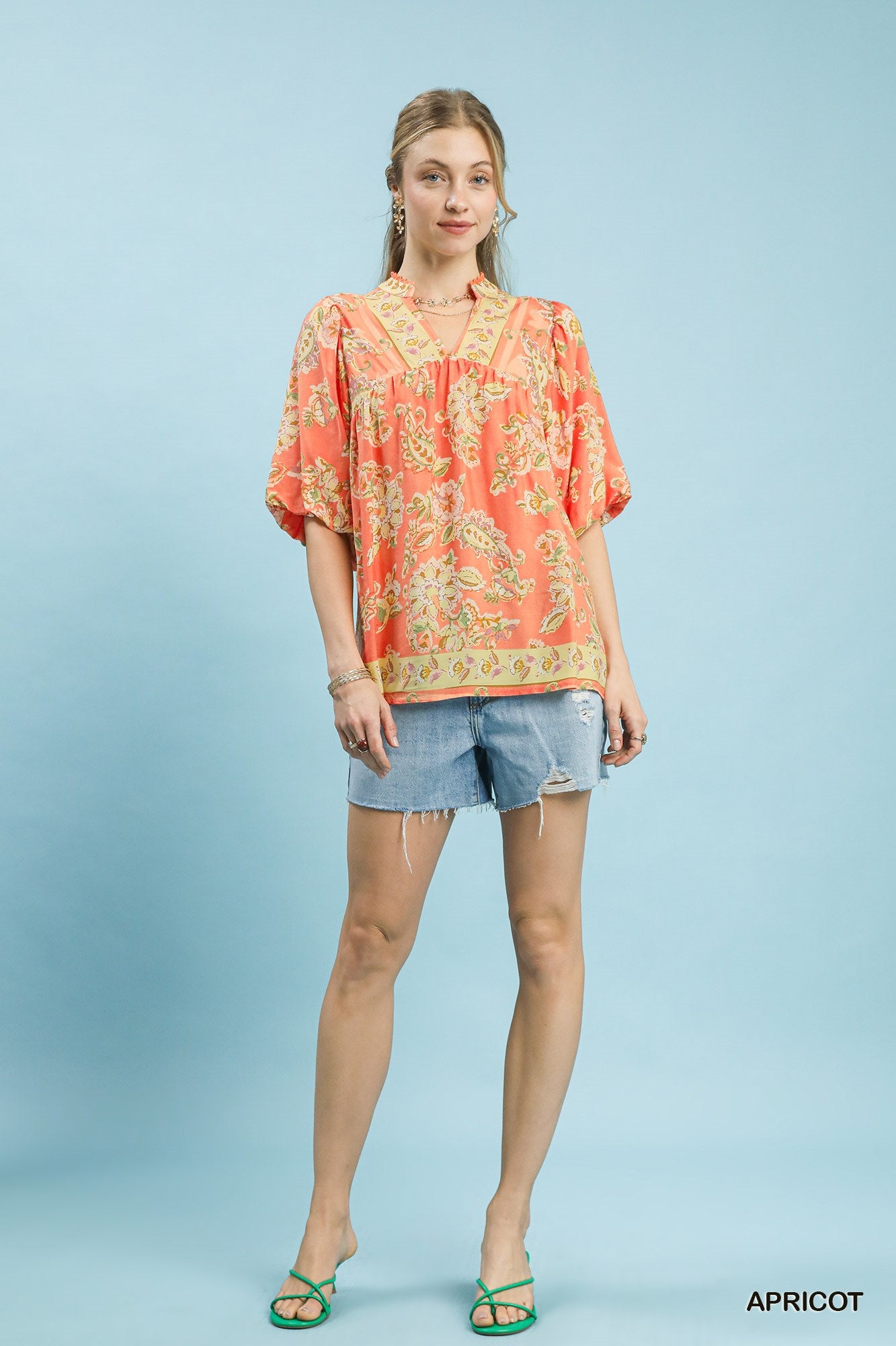 Woman wearing a patterned orange shirt and denim shorts on a light blue background