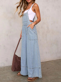 Woman wearing light blue denim overalls against a plain background