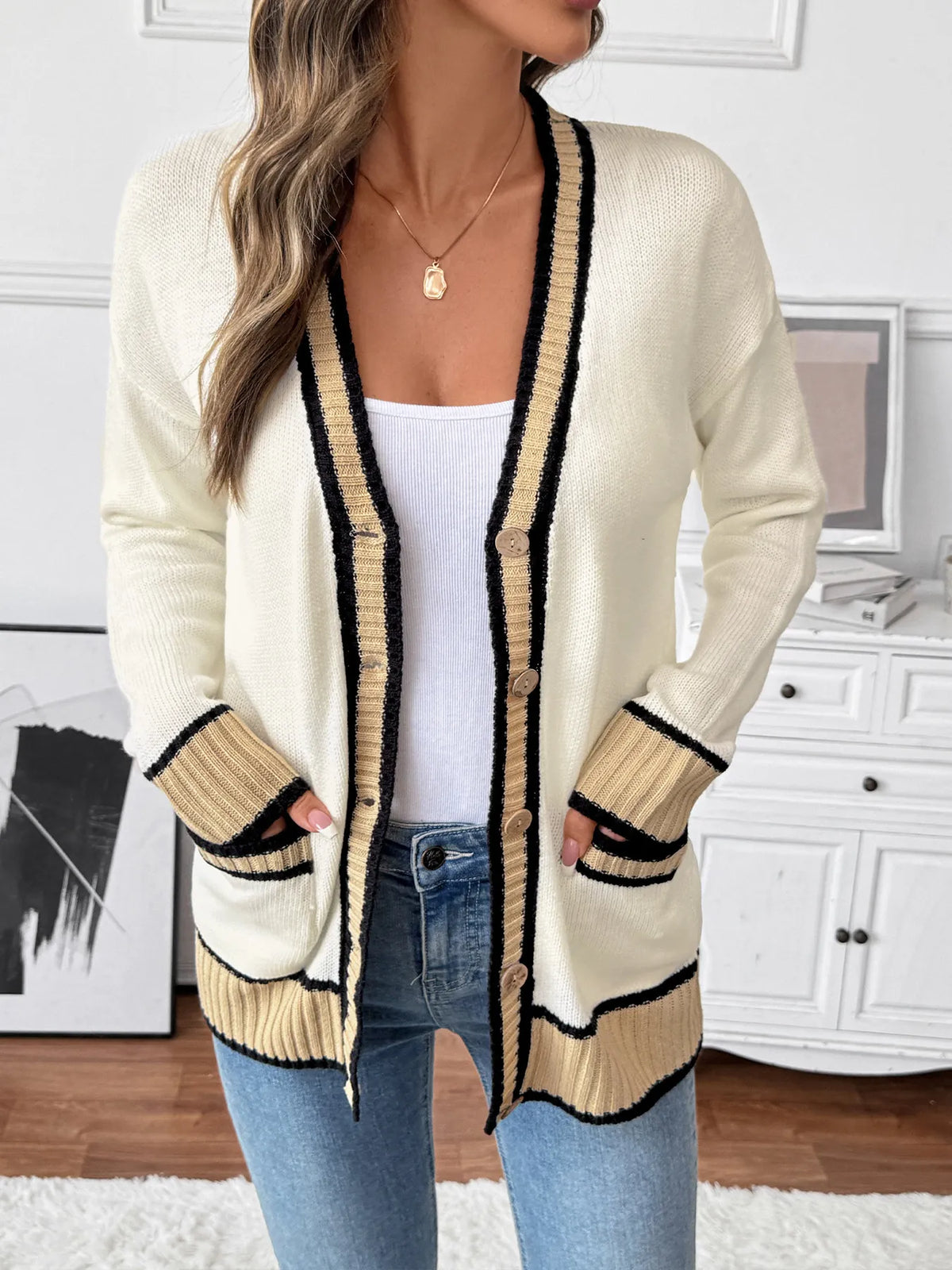 Woman wearing a cream cardigan with black trim in a room setting.