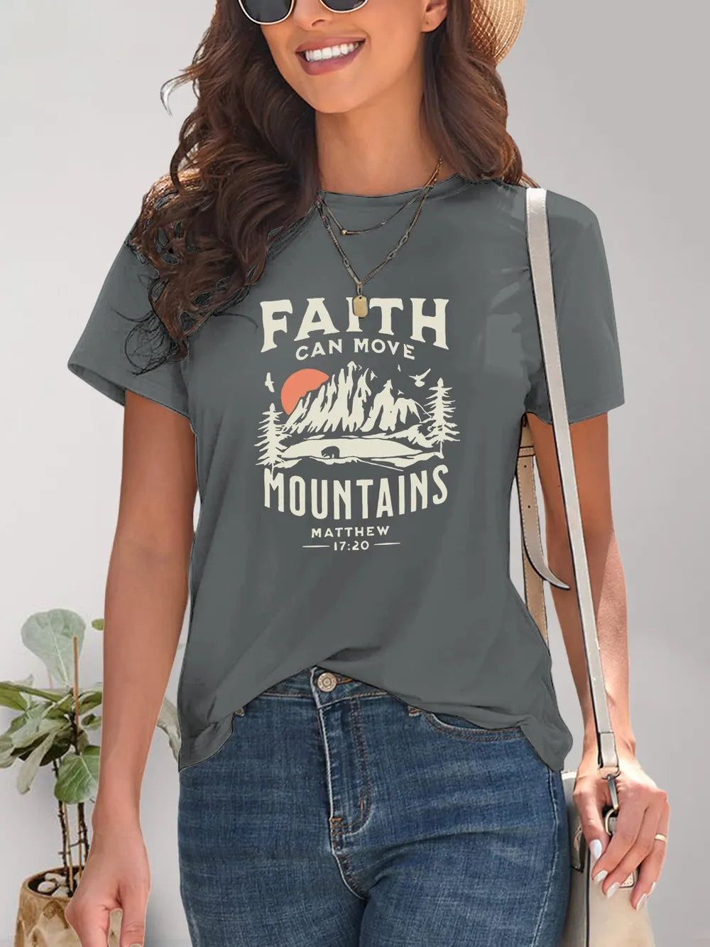 Woman wearing a gray t-shirt with 'Faith Can Move Mountains' graphic and text.