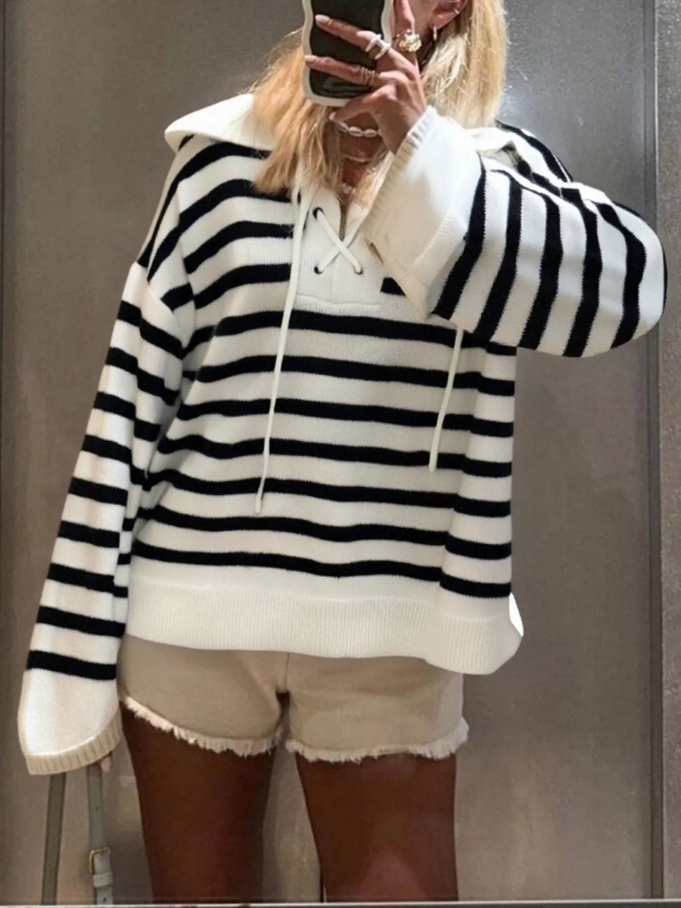 Person wearing a black and white striped hoodie and white shorts, taking a mirror selfie.