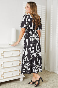Woman wearing a black and white patterned dress standing in a room with white furniture.