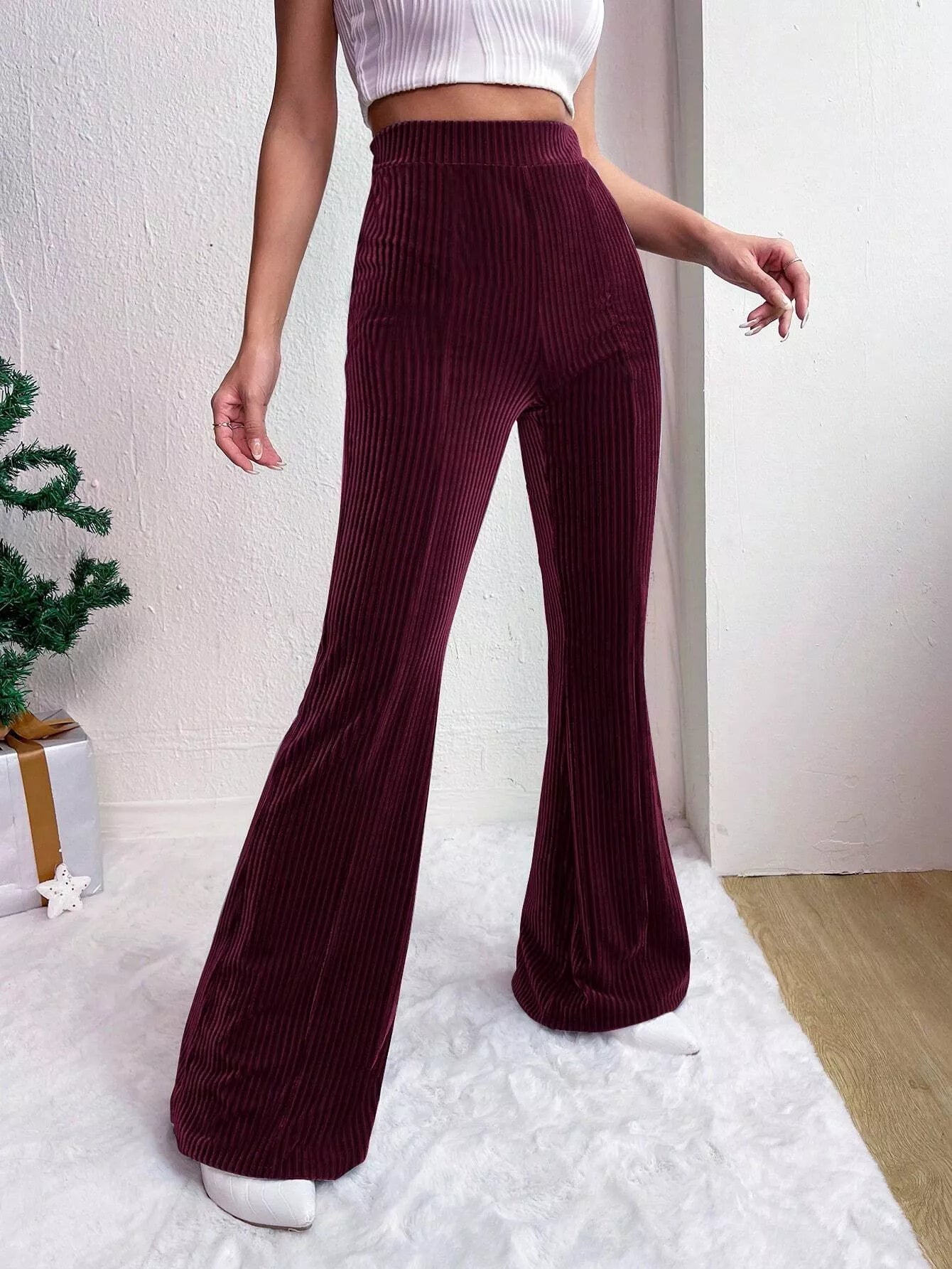 Person wearing maroon ribbed flared pants with a white top and shoes indoors.