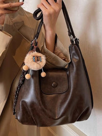 Brown handbag with a decorative keychain held by a person wearing a beige coat.