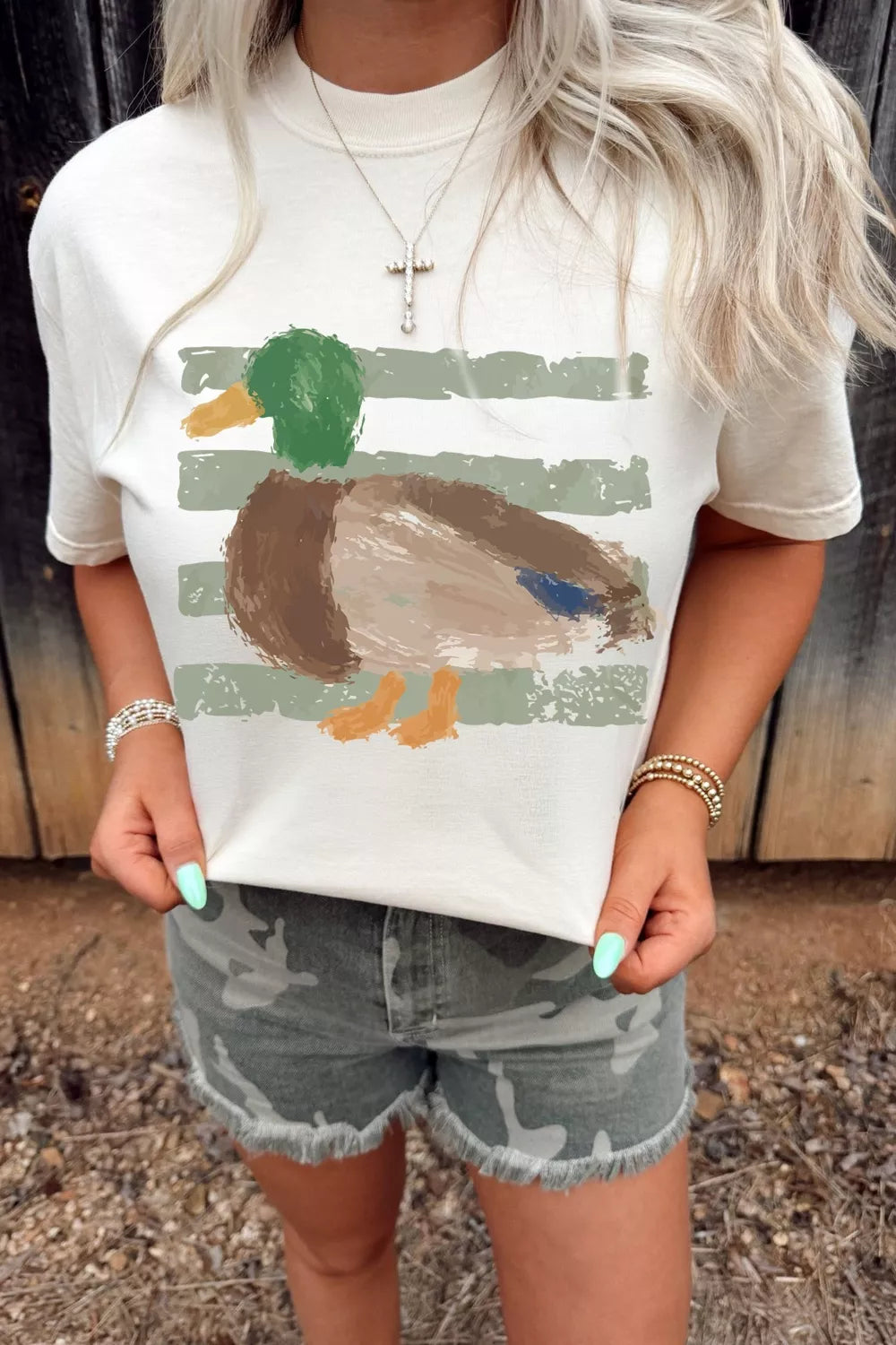 Person wearing a white t-shirt with a duck graphic and camouflage shorts outdoors.