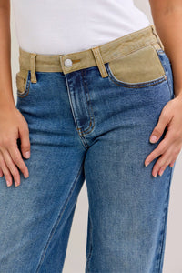 Person wearing blue jeans with a beige belt and white shirt on a plain background