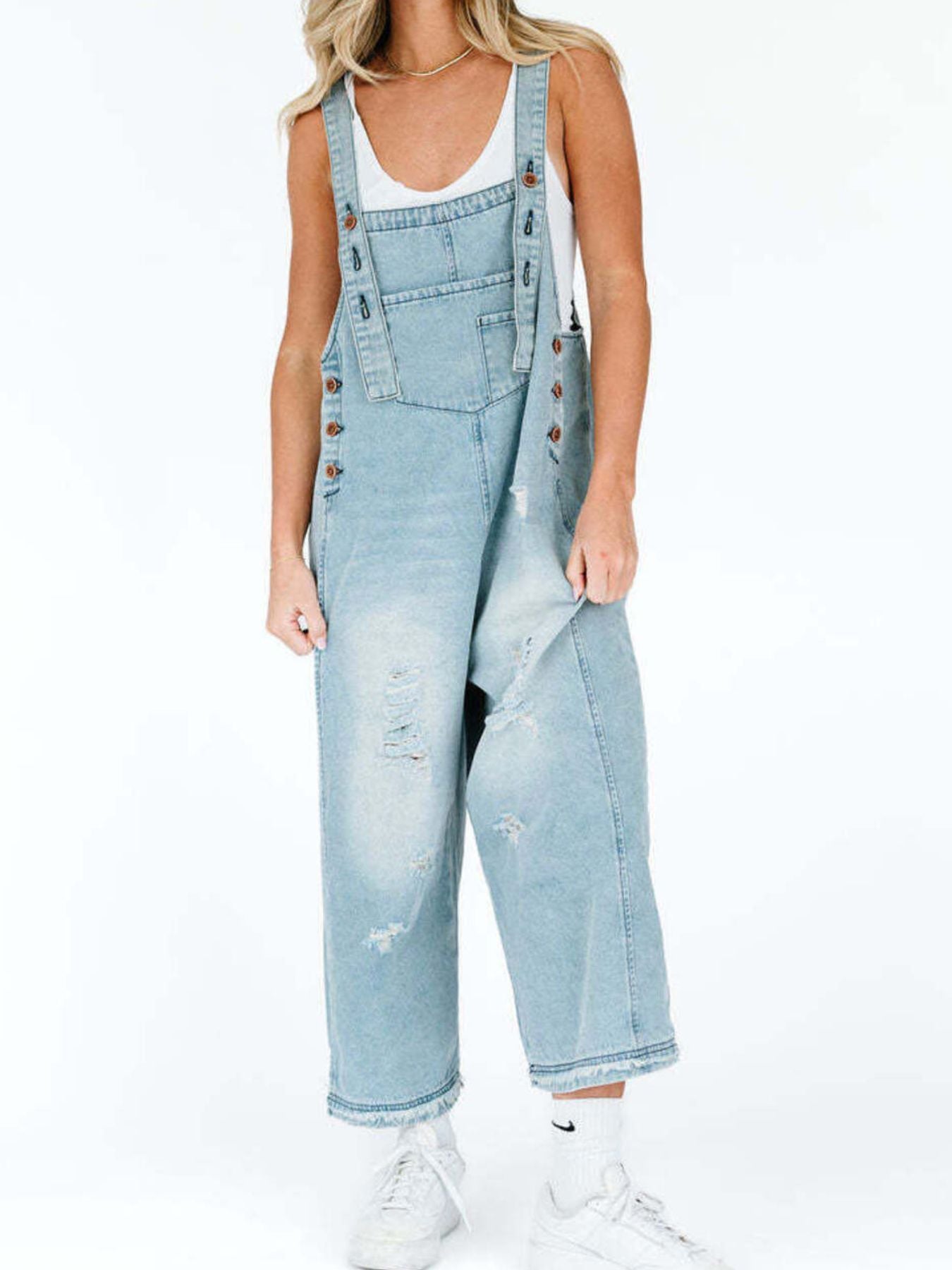 Person wearing light blue denim overalls on a white background