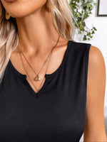 Close-up of a person wearing a black sleeveless top and gold necklaces with a blurred background.