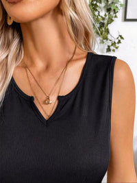Close-up of a person wearing a black sleeveless top and gold necklaces with a blurred background.