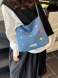Person holding a blue tote bag with colorful polka dots indoors.