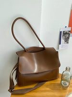 Brown leather handbag on a wooden surface with a white wall background