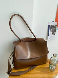 Brown leather handbag on a wooden surface with a white wall background