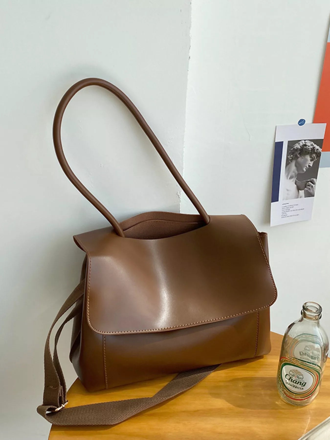 Brown leather handbag on a wooden surface with a white wall background