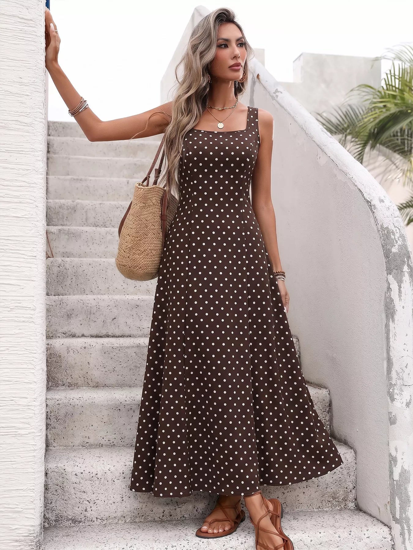 Woman in a brown polka dot dress standing on a staircase with a neutral background