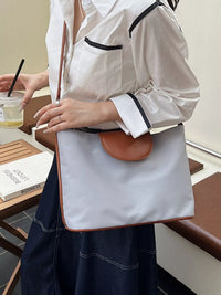 Person holding a white tote bag with brown leather patch in an indoor setting
