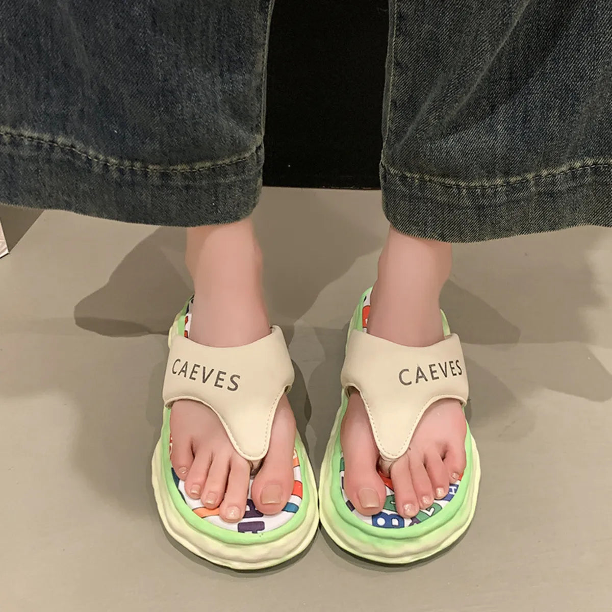 Beige sandals with colorful soles worn by a person in dark jeans.