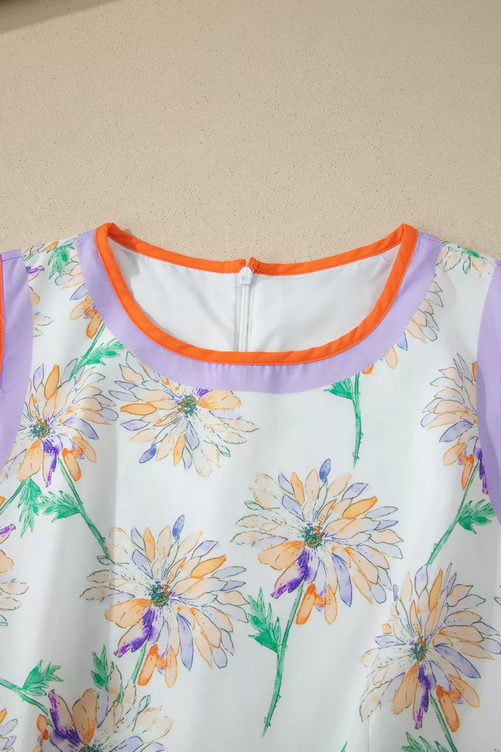 Close-up of a floral dress with a purple neckline against a beige background
