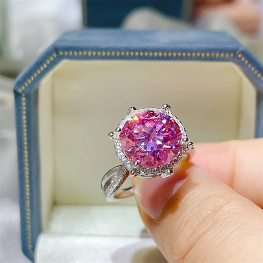 Pink gemstone ring held by a hand with a blurred background