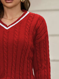 Close-up of a person wearing a red cable knit sweater with a blurred background