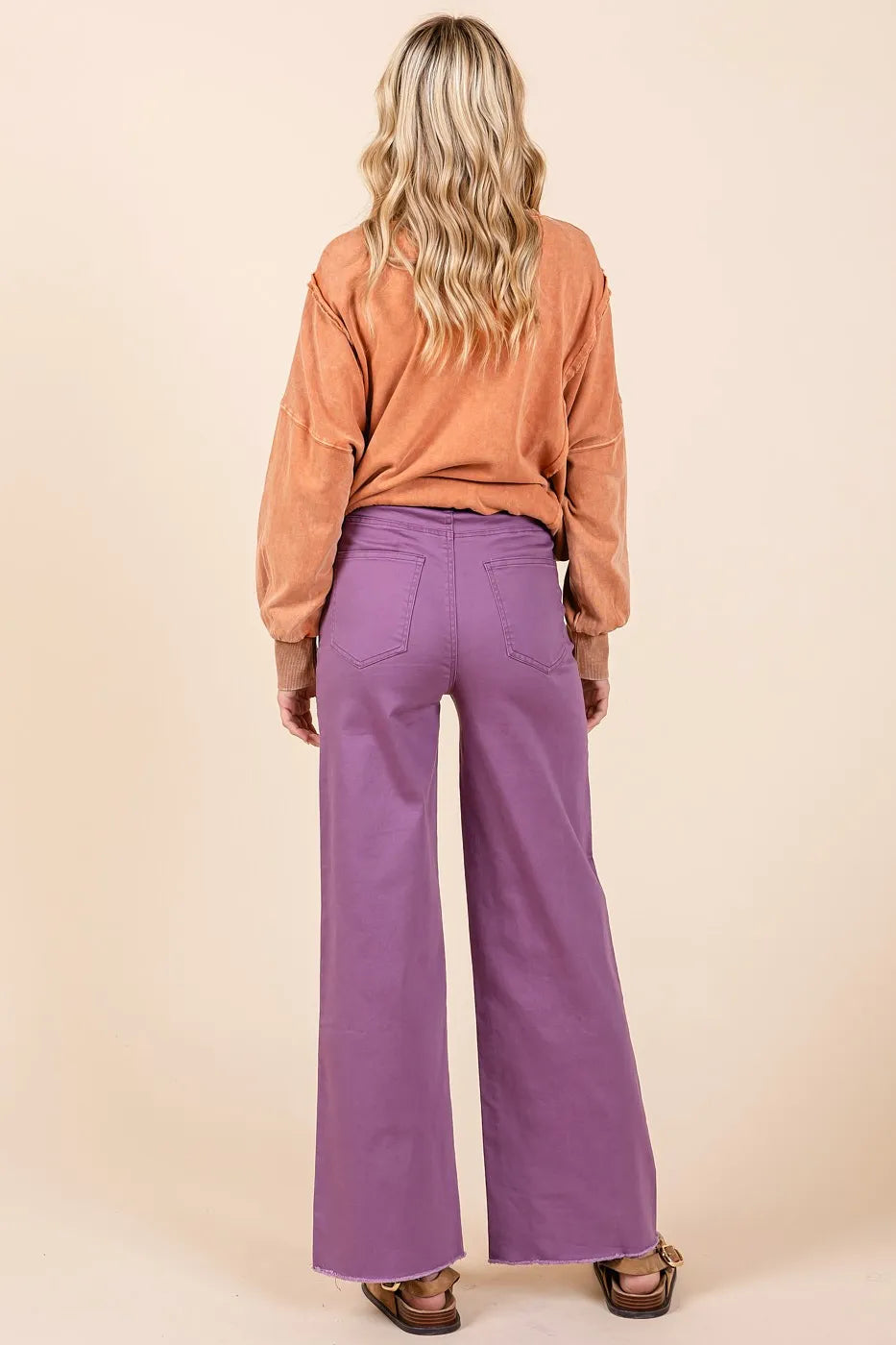 Person wearing a brown top and purple pants on a beige background