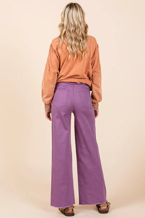 Person wearing a brown top and purple pants on a beige background