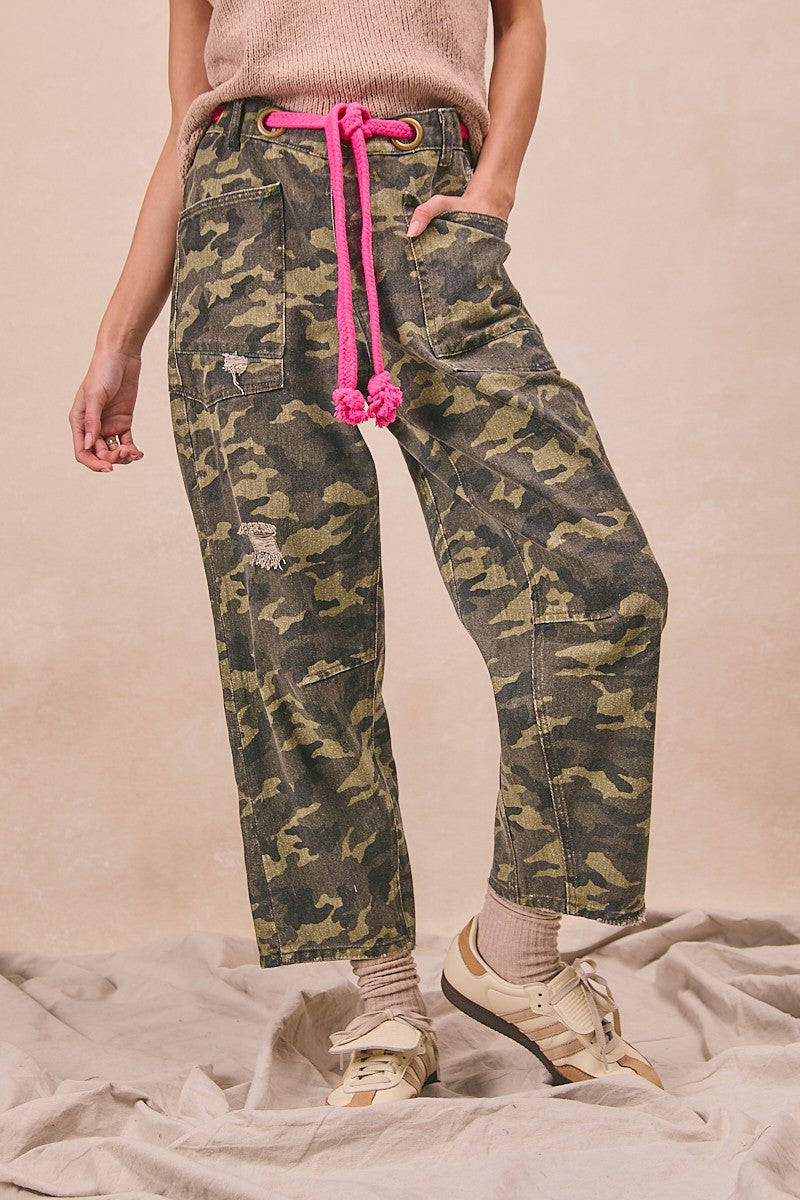 Camouflage pants with pink drawstring worn by a person on a beige background