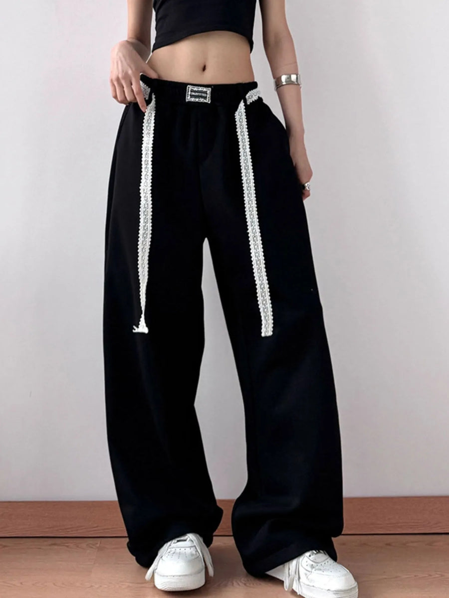 Person wearing black wide-leg pants with white drawstrings on a plain background