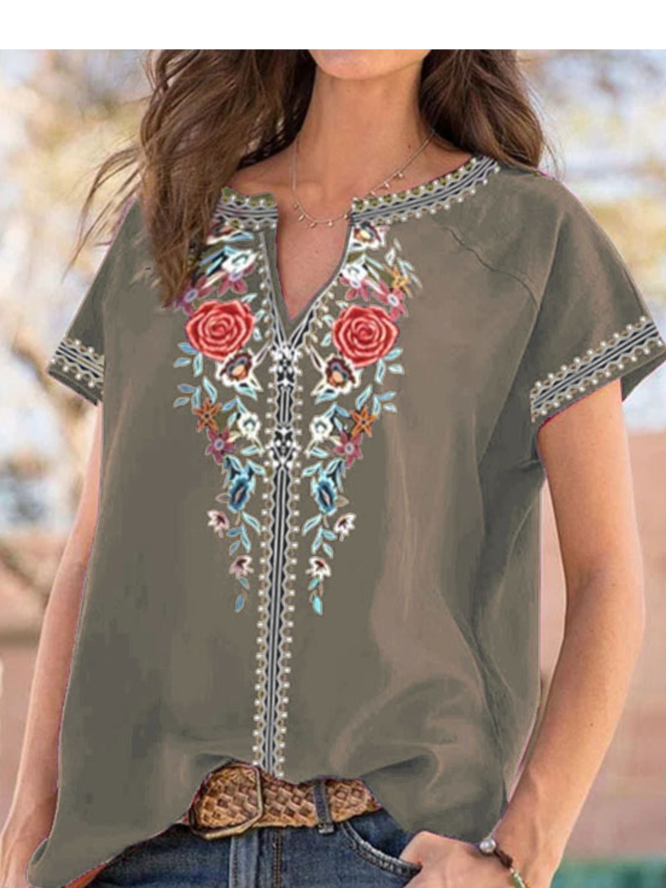 Woman wearing an olive green blouse with floral embroidery and a belt, standing outdoors.