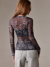 Woman wearing a sheer leopard print top and light gray pants against a neutral background