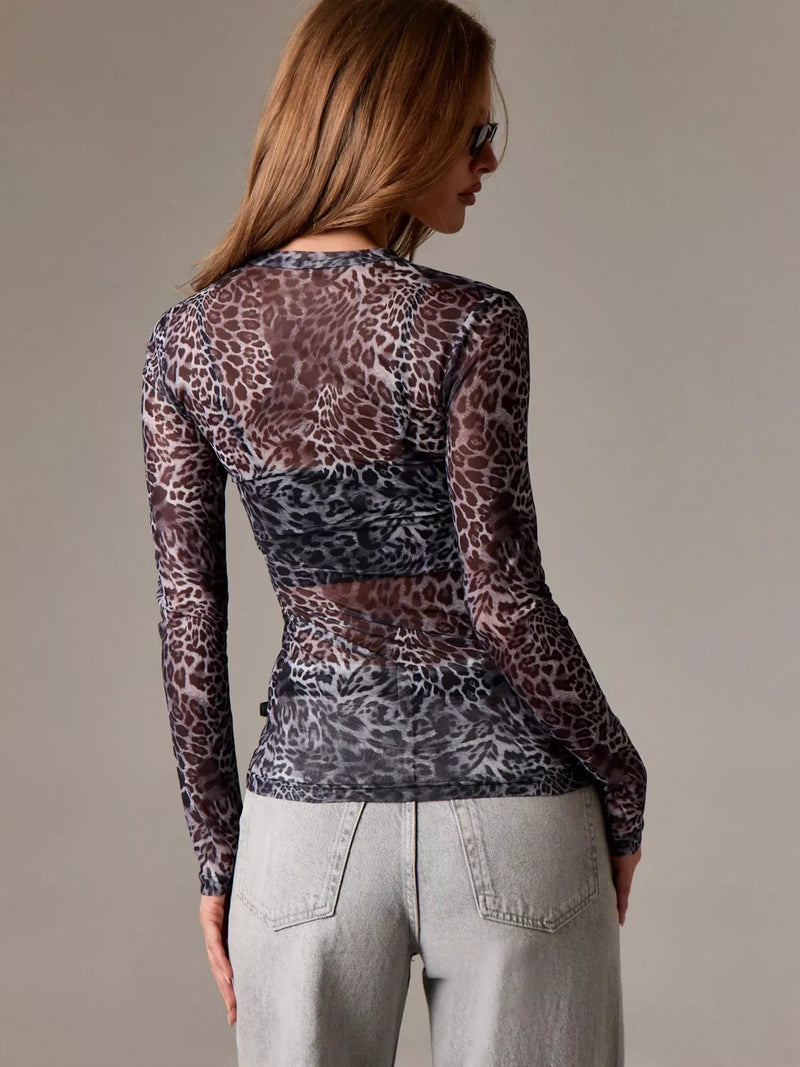 Woman wearing a sheer leopard print top and light gray pants against a neutral background