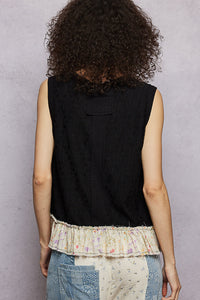 Person wearing a black sleeveless top with a textured pattern and a patchwork skirt against a gray background