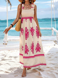 Woman in a beige dress with pink patterns standing on a beach.