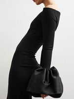 Person wearing a black off-shoulder dress holding a matching black clutch against a white background