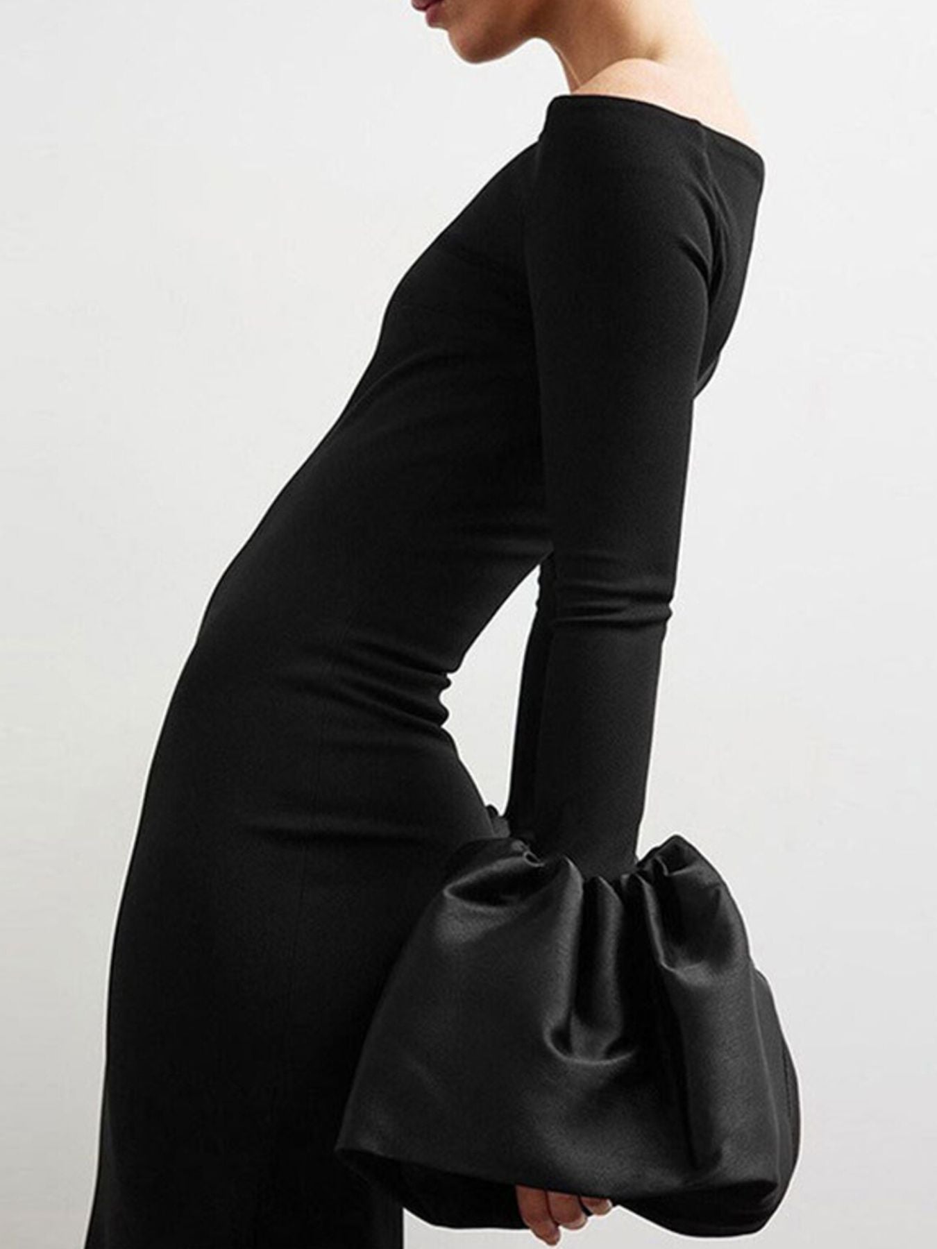 Person wearing a black off-shoulder dress holding a matching black clutch against a white background