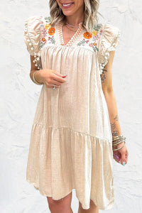 Woman wearing a beige dress with floral embroidery against a white background
