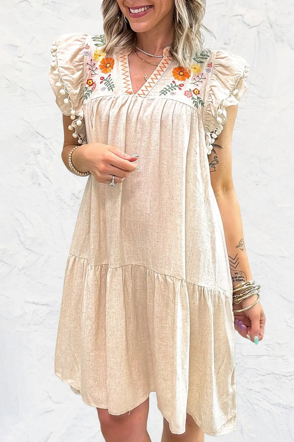 Woman wearing a beige dress with floral embroidery against a white background