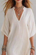 Woman wearing a white blouse with layered necklaces and bracelets on a plain background
