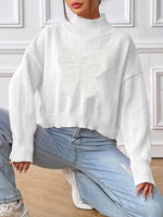 Person wearing a white turtleneck sweater and light blue jeans in a room with white walls.