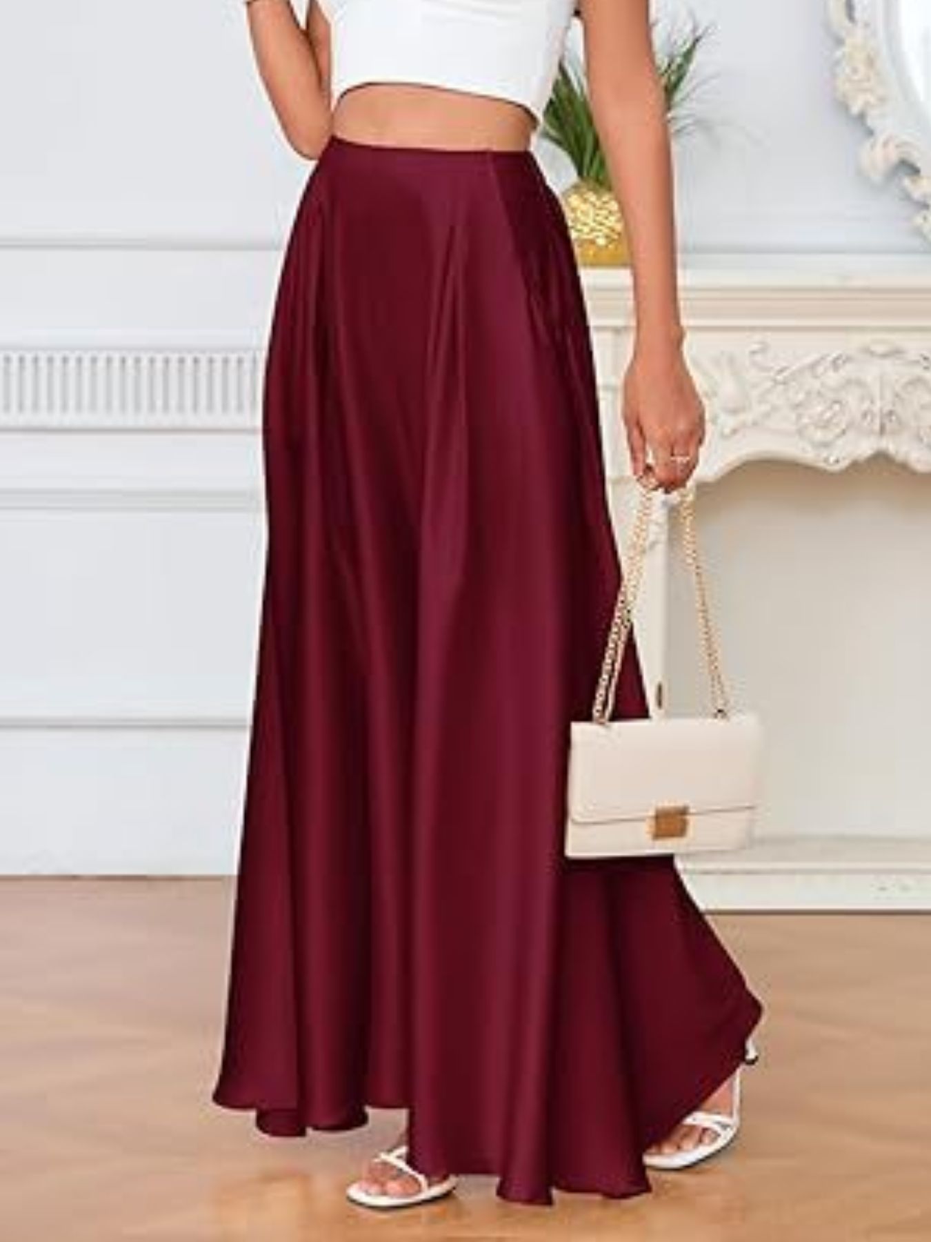 Person wearing a burgundy skirt and white top, holding a white handbag indoors.
