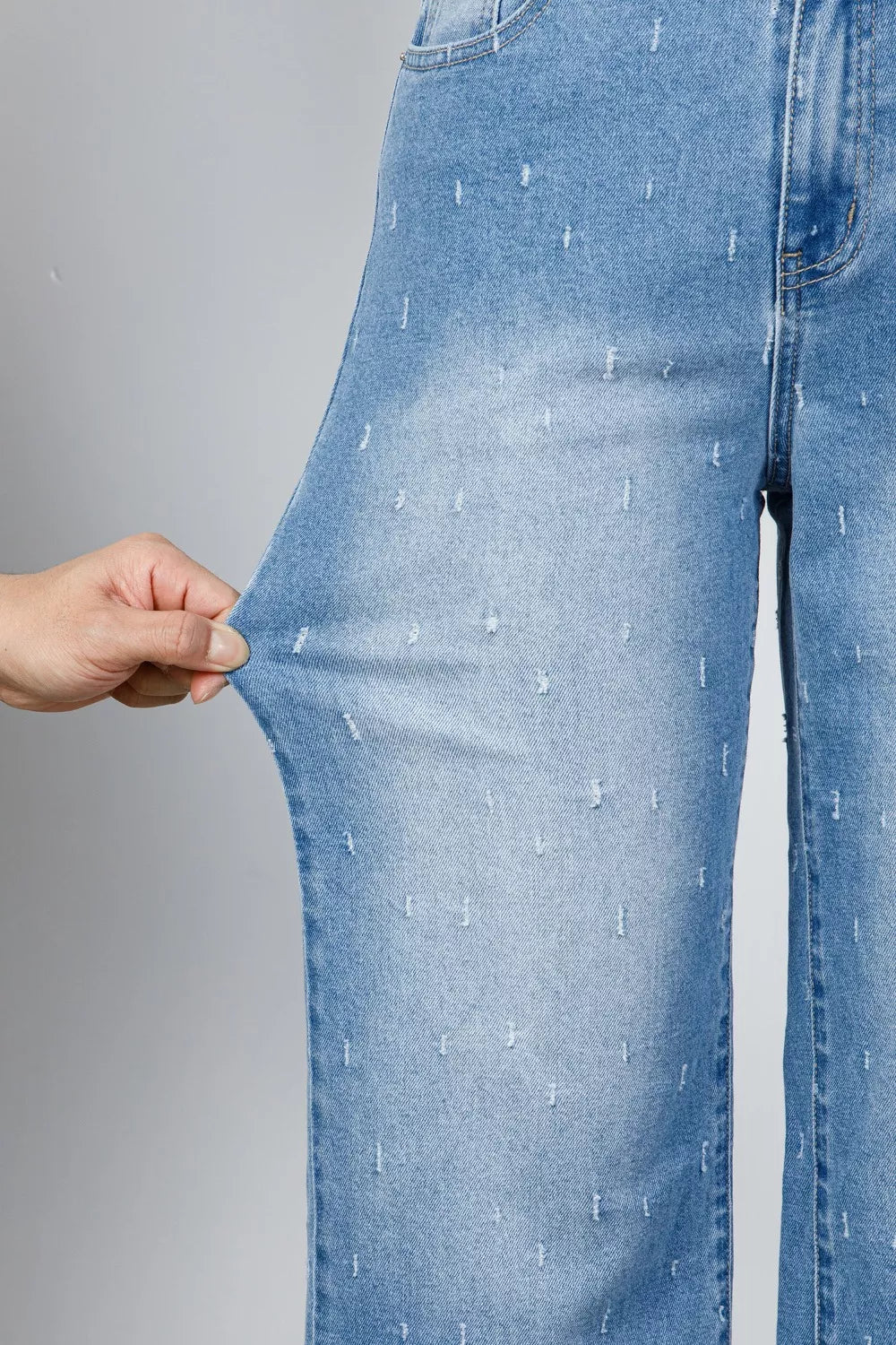 Close-up of blue jeans being stretched with a hand on a gray background